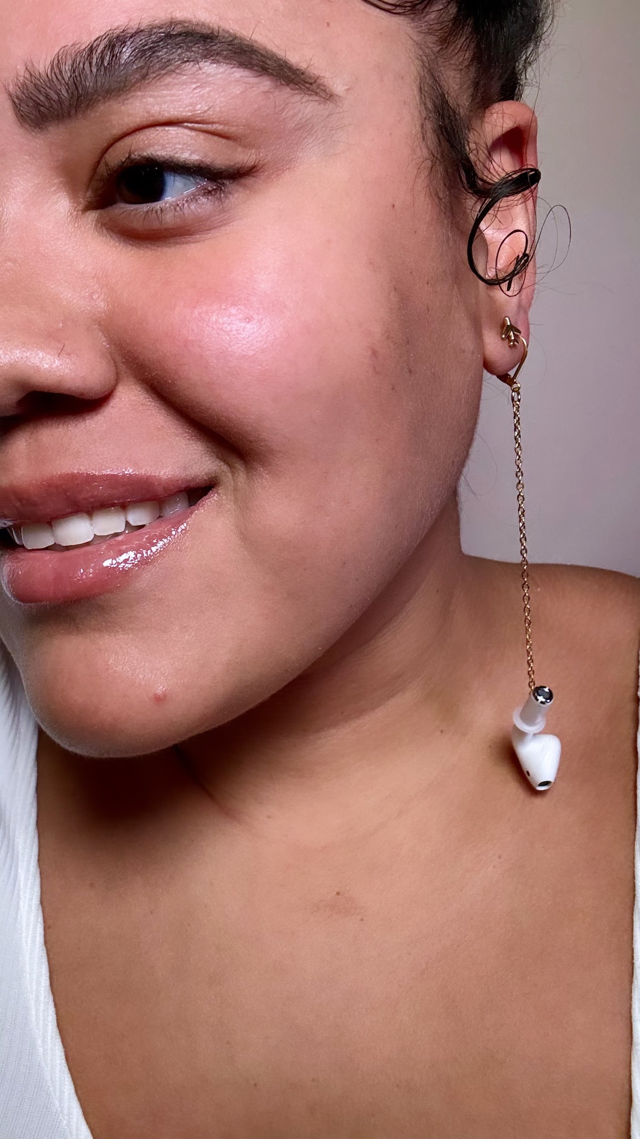 Close-up of a person wearing a unique earring with a Bluetooth attached a gold chain.