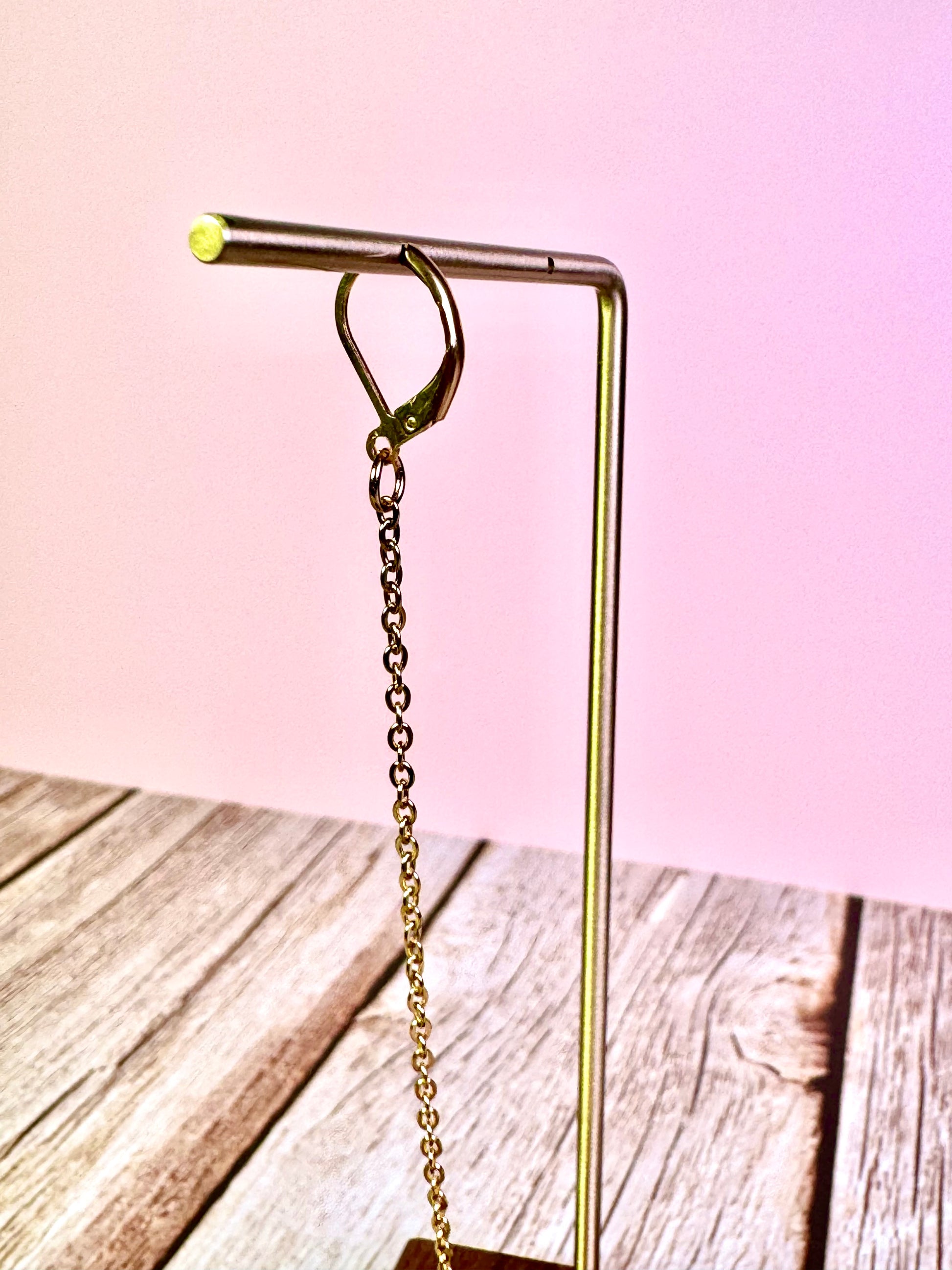 Gold metal hook with chain on a wooden surface and pink background