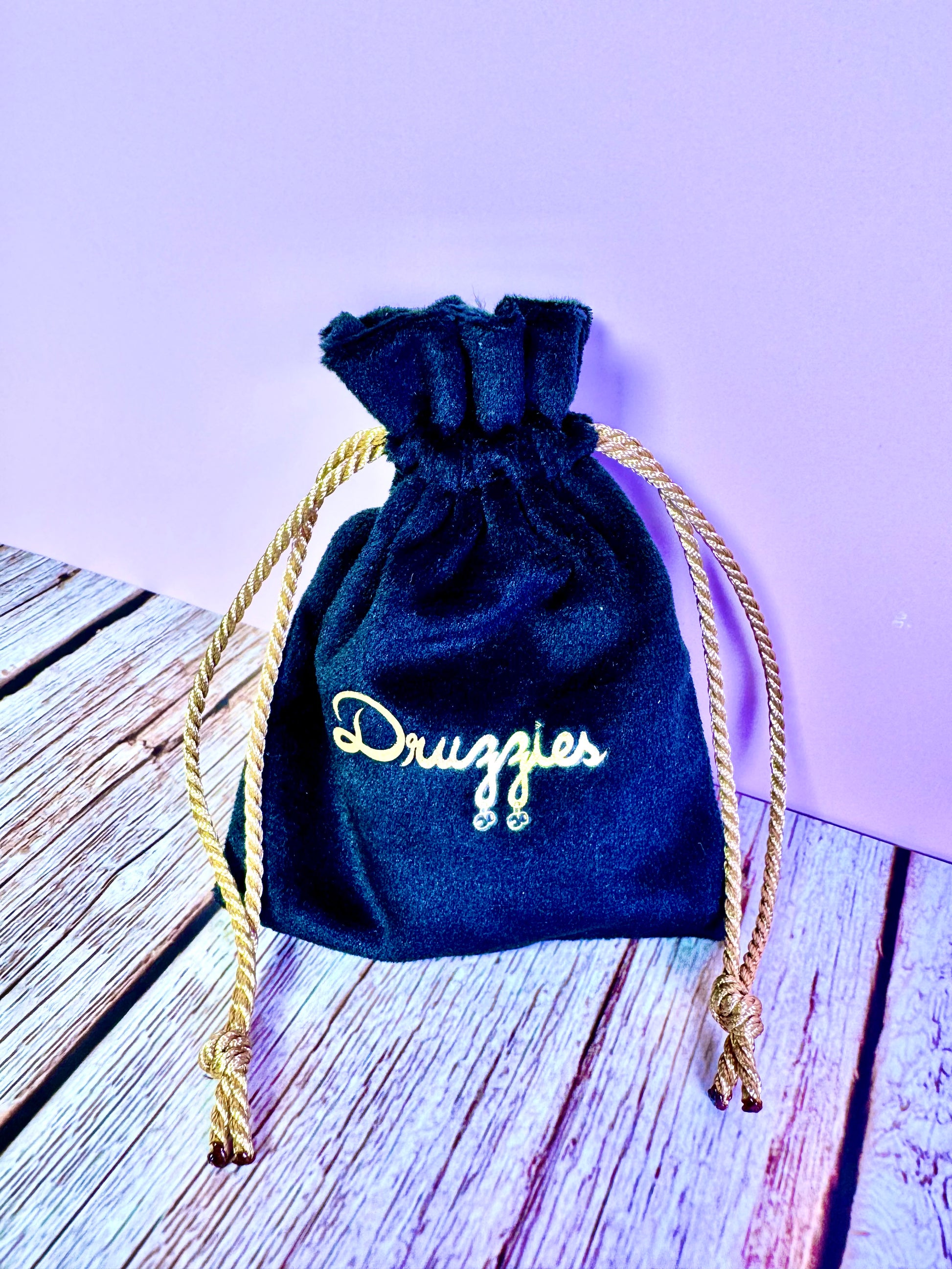 Black velvet with gold rope drawstring bag with 'Druzzies' text on a wood surface
